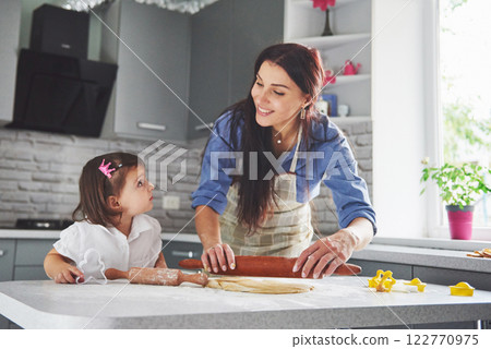 Happy family in the kitchen. Holiday food concept. Mother and daughter preparing the dough, bake cookies. Happy family in making cookies at home. Homemade food and little helper 122770975