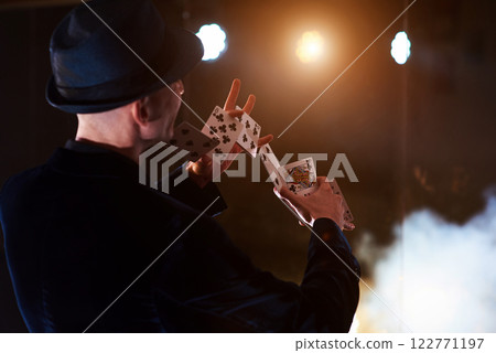 Magician showing trick with playing cards. Magic or dexterity, circus, gambling. Prestidigitator in dark room with fog 122771197