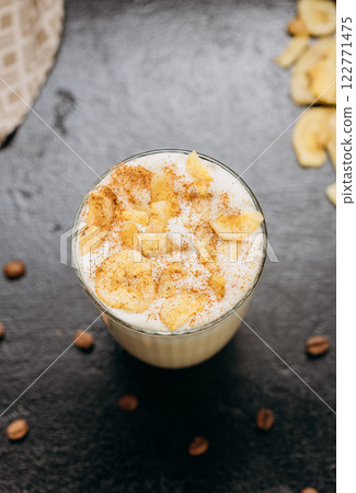 Creamy latte with whipped foam, dried apple slices, and cinnamon, served on a dark textured surface 122771475
