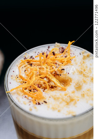 Gourmet layered latte with whipped foam, orange zest, and spices, served on a rustic dark surface 122771496