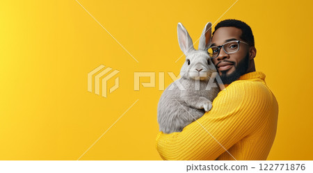 Portrait of a stylish African man in a yellow sweater holding a fluffy grey rabbit against a vibrant yellow background. A heartwarming image symbolizing care, joy, and the bond with pets. Portrait of a stylish African man in a yellow sweater holding a fluffy grey rabbit against a vibrant yellow background. A heartwarming image symbolizing care, joy, and the bond with pets. 122771876