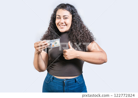 Smiling girl holding a 100 dollar bill gesturing approved. Young woman holding a 100 dollar bill with thumb up 122772824