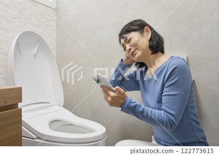 A woman checking repairman on her smartphone in the toilet A woman checking repairman on her smartphone in the toilet 122773615