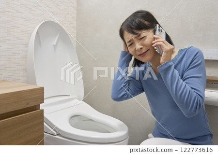 A woman calling a repairman in the bathroom A woman calling a repairman in the bathroom 122773616