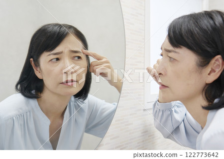 A woman in her 50s worries about wrinkles on her forehead in the mirror 122773642