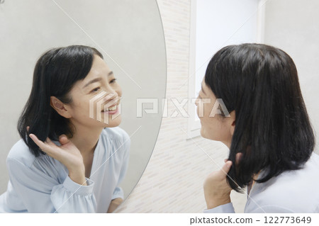 A woman in her 50s styling her hair in the mirror A woman in her 50s styling her hair in the mirror 122773649