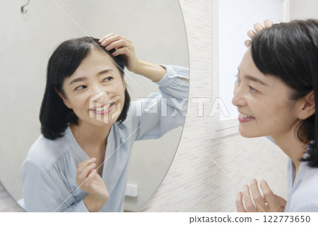 A woman in her 50s styling her hair in the mirror 122773650
