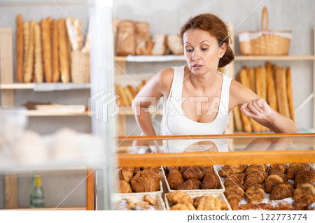 Young European woman near window of bakery food court store examines assortment 122773774