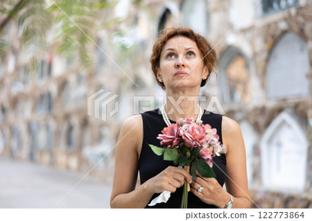 Upset woman in black dress, who lost loved one, brings flowers to grave Upset woman in black dress, who lost loved one, brings flowers to grave 122773864