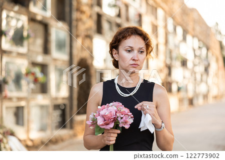 Drieving woman in black dress standing with bouquet by columbarium 122773902