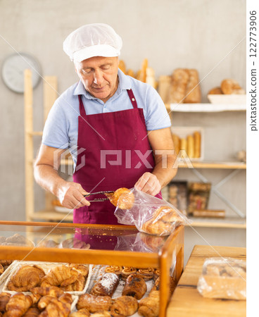 Elderly man seller puts croissants in bag Elderly man seller puts croissants in bag 122773906