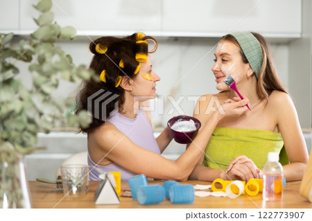 Relaxed female friends applying facial mask to each other at home 122773907