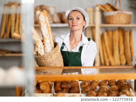 Female baker worker sells baguette, shows many products Female baker worker sells baguette, shows many products 122773938