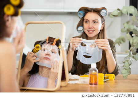 Two women testing out hydrating face paper mask at home 122773991