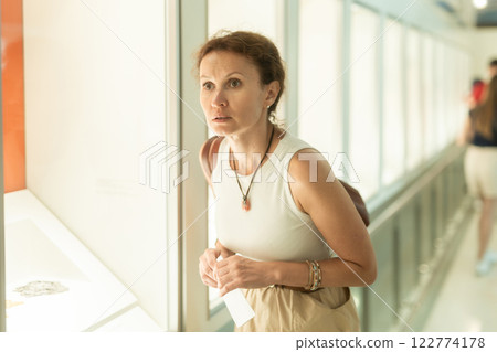 Attentive woman standing near exposition and looking with interest at art objects under glass in museum Attentive woman standing near exposition and looking with interest at art objects under glass in museum 122774178