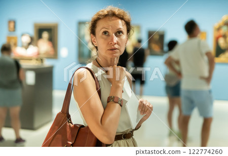 Portrait of beautiful woman looking at pictures and amaze in museum, holding guide book Portrait of beautiful woman looking at pictures and amaze in museum, holding guide book 122774260