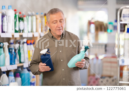 Male shopper carefully selects a spray glass cleaner for windows in home Male shopper carefully selects a spray glass cleaner for windows in home 122775061
