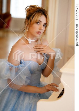 Elegant woman in a light blue ball gown in a luxurious classic interior plays a white piano Elegant woman in a light blue ball gown in a luxurious classic interior plays a white piano 122775782