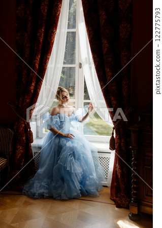 Portrait of an elegant woman in a light blue ball gown in a classic interior by a large window 122775793