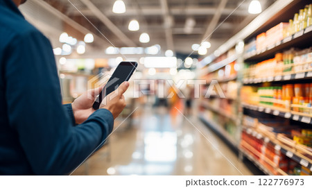 Mobile phone in hand inside super market. Close-up of a hand holding a smartphone with a mobile screen Mobile phone in hand inside super market. Close-up of a hand holding a smartphone with a mobile screen 122776973