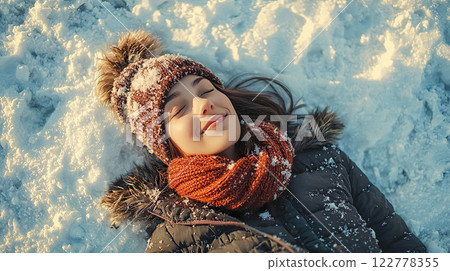 Young Caucasian woman lying on the snow with her eyes closed 122778355