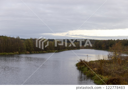 autumn landscape in cloudy weather with a lake and deciduous trees autumn landscape in cloudy weather with a lake and deciduous trees 122778483