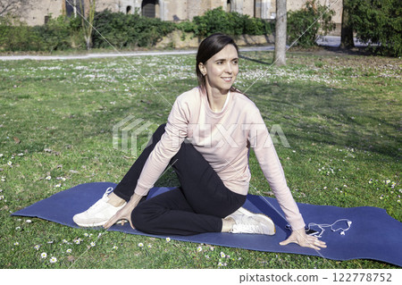 Portrait of beautiful young woman with long hair doing yoga on mat in the city park. The concept of a healthy lifestyle. Outdoors yoga. Healthy lifestyle concept, sports, fitness, yoga. 122778752