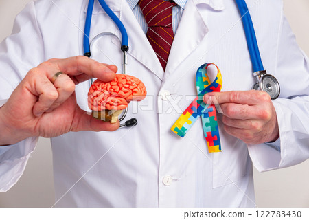 World Autism awareness and pride day. Doctorwith model human brain with Puzzle pattern ribbon in hand World Autism awareness and pride day. Doctorwith model human brain with Puzzle pattern ribbon in hand 122783430