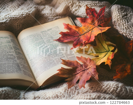 Warm autumn composition with vibrant fall leaves, an open book, and a soft knitted blanket. Cozy reading nook concept 122784663