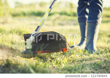 worker mows green grass on the lawn with hand trimmer. lawn care. weed control. Woman with gasoline mower cutting grass. Grass trimmer worker, garden work. 122784843