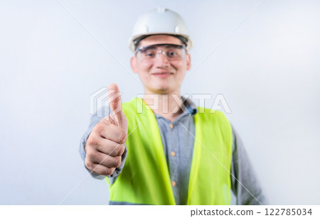 Smiling young engineer gesturing approval with thumb. Cheerful engineer giving thumbs up to the camera isolated 122785034