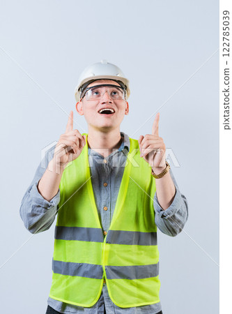 Surprised young architect pointing up. Amazed engineer pointing at an advertisement. Engineer with astonished face pointing at blank space 122785039