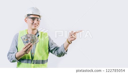 Smiling young engineer holding money pointing aside isolated. Handsome male engineer showing money pointing an advertisement isolated Smiling young engineer holding money pointing aside isolated. Handsome male engineer showing money pointing an advertisement isolated 122785054