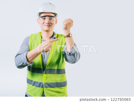 Smiling engineer pointing at his wrist watch isolated. Young engineer pointing and showing his wrist watch Smiling engineer pointing at his wrist watch isolated. Young engineer pointing and showing his wrist watch 122785065