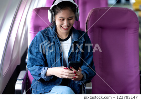 young woman traveling alone on airline uses smartphone and headphones young woman traveling alone on airline uses smartphone and headphones 122785147