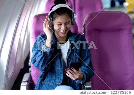 young woman traveling alone on airline uses smartphone and headphones 122785169