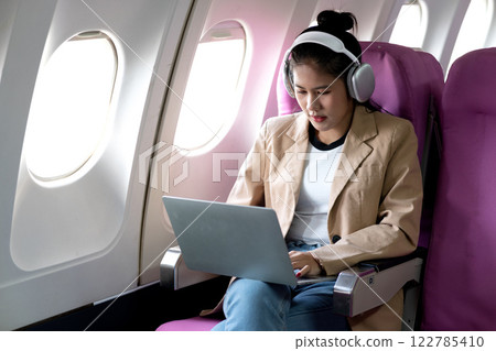 young woman is using a laptop and wireless headphones while traveling 122785410