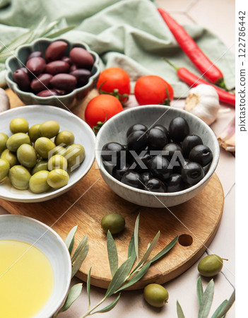 Black and green olives with tomatoes, garlic, chili peppers and olive oil on kitchen table Black and green olives with tomatoes, garlic, chili peppers and olive oil on kitchen table 122786442