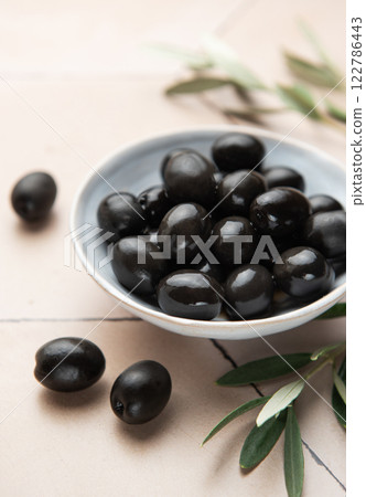 Black olives served in ceramic bowl on hexagonal beige tiles, decorated with olive tree branch Black olives served in ceramic bowl on hexagonal beige tiles, decorated with olive tree branch 122786443