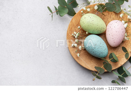 Pastel easter eggs on wooden plate with eucalyptus 122786447