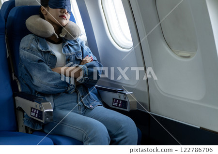 young woman travels alone on a plane and uses an eye mask 122786706