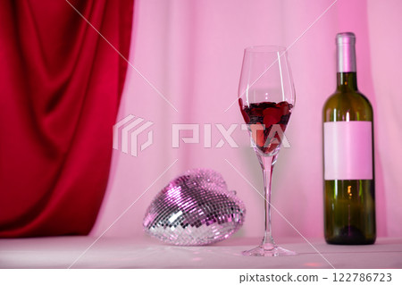 Wine glass with heart confetti, bottle, and disco on pink background 122786723