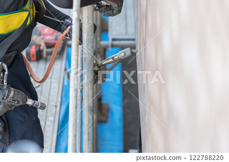 [Large-scale apartment building repair work: Workers connecting wall ties and building scaffolding] 122788220