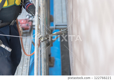 [Large-scale apartment building repair work: Workers connecting wall ties and building scaffolding] 122788221