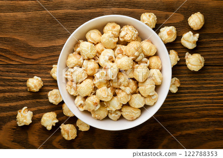 Caramel popcorn in a plate on a wooden background. Top view 122788353