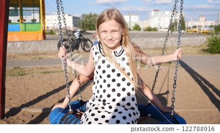 A cheerful young girl swings back and forth with joy and laughter on a bright sunny day at a vibrant playground A cheerful young girl swings back and forth with joy and laughter on a bright sunny day at a vibrant playground 122788916