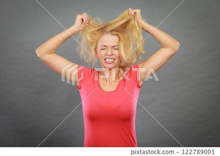 Frustrated woman holding her damaged blonde hair Frustrated woman holding her damaged blonde hair 122789001