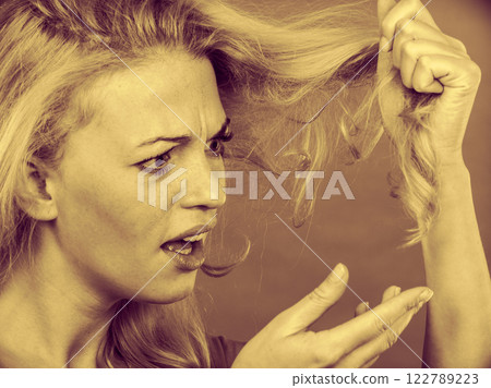 Sad woman looking at damaged hair ends 122789223