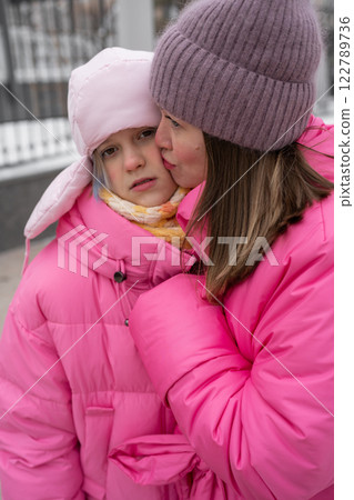 Mother and Her Adorable Daughter Embracing Each Other in Stylish Pink Winter Fashion, relationship with a teenager. 122789736