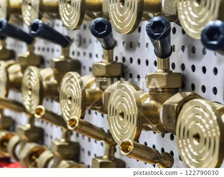 Detailed view of brass valves and fittings arranged on a pegboard in a workshop setting 122790030